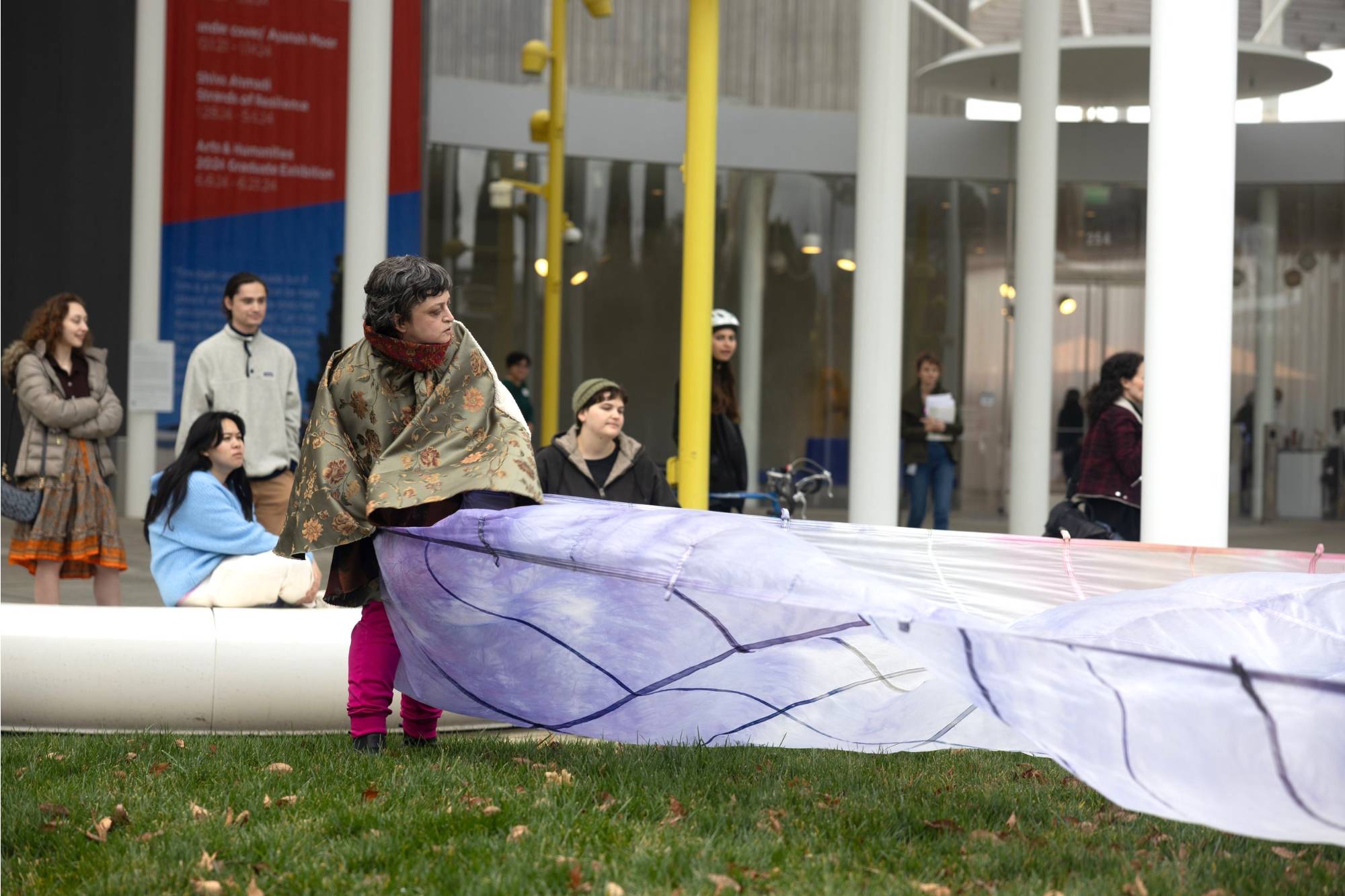 Performance in front of building where a person is pulling a large light purple leaf-like surface.